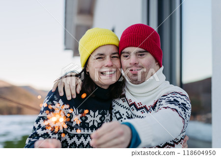 The mother and young man with Down syndrome are outside, having fun with Christmas sparklers and enjoying first snow 118604950