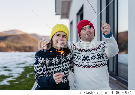 The mother and young man with Down syndrome are outside, having fun with Christmas sparklers and enjoying first snow The mother and young man with Down syndrome are outside, having fun with Christmas sparklers and enjoying first snow 118604954