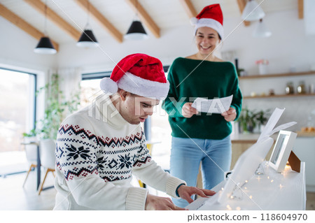 Young man with Down syndrome learning to play christmas songs on piano, mother singing. Concept of peaceful Christmas family moment. 118604970