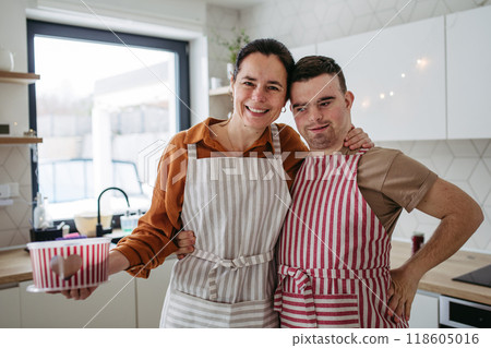 Portrait of man with Down syndrome and his mom with cookie tin full of Christmas gingerbread cookies. Peaceful Christmas moment for man with Down syndrome. 118605016