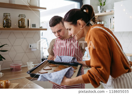 Young man with Down syndrome and his mom baking Christmas gingerbread cookies. Christmas peaceful moment for man with Down syndrome. Young man with Down syndrome and his mom baking Christmas gingerbread cookies. Christmas peaceful moment for man with Down syndrome. 118605035