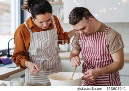 Young man with Down syndrome and his mom preparing dough for Christmas cookies. Christmas peaceful moment for man with Down syndrome. Young man with Down syndrome and his mom preparing dough for Christmas cookies. Christmas peaceful moment for man with Down syndrome. 118605041