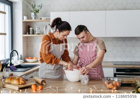 Young man with Down syndrome and his mom preparing dough for Christmas cookies. Christmas peaceful moment for man with Down syndrome. 118605056