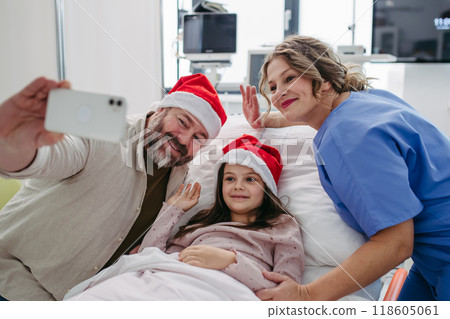 Nurse, father and daughter on hospital bed taking selfie. Sick little girl spending Christmas in hospital Nurse working shift on Christmas Eve. 118605061