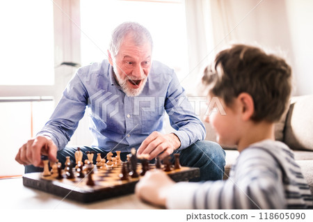 Grandpa teaching young boy to play chess. Grandfather spending time with grandson, taking care of him while parents are at work. Grandpa teaching young boy to play chess. Grandfather spending time with grandson, taking care of him while parents are at work. 118605090