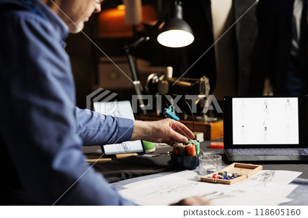 Senior couturier preparing his atelier shop workspace before starting work on upcoming runway fashion show collection. Tailor picking necessary sewing materials for customer comissioned outfit Senior couturier preparing his atelier shop workspace before starting work on upcoming runway fashion show collection. Tailor picking necessary sewing materials for customer comissioned outfit 118605160