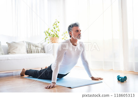 Handsome man exercising at home on gym mat. doing yoga. Routine home workout for a middle-aged man. 118605313