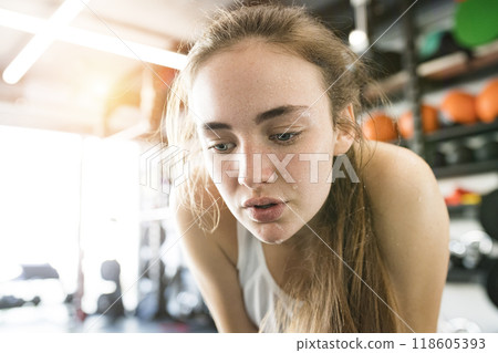 Young fitness girl with sweat on face feeling exhausted after hard workout in gym, holding knees, breathing. 118605393
