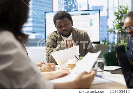 Business professionals engage in a strategy session for a new project, utilizing documents with data analytics to develop innovative solutions to improve the market presence. Conference table. 118605413