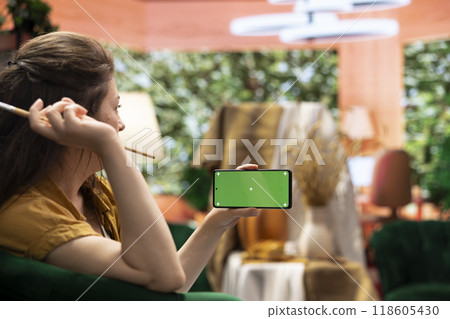 Female artist holding device with green screen in art and craft atelier, admiring her rustic artwork painted with watercolor paint. Woman preparing a masterpiece for an art gallery exhibition. 118605430