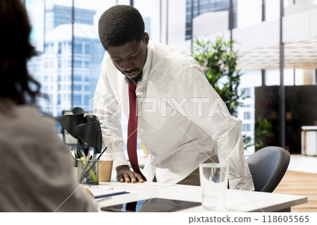 HR staff member negotiating job offers and salary packages with candidate after successful interview. Manager in inclusive workspace analyzing african american man resume and cover letter 118605565