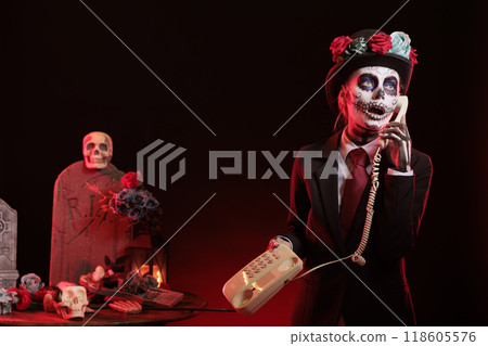 Lady talks on cord telephone at religious processions during Dia de los Muertos holiday. Woman uses landline phone to answer call,, wearing skeleton makeup symbolizing reverence for deceased Lady talks on cord telephone at religious processions during Dia de los Muertos holiday. Woman uses landline phone to answer call,, wearing skeleton makeup symbolizing reverence for deceased 118605576