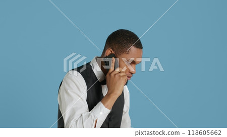 Hotel porter in tuxedo making reservations on phone call in studio, discussing with future guests about lodging and amenities. Doorkeeper hotelier on telephone line. Camera A. 118605662