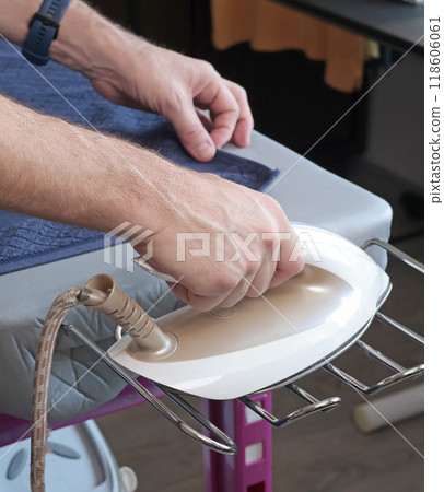 Man irons towel and clothes with steam iron on modern ironing table. Cleanliness and care of clothes at home. Household appliances. Man irons towel and clothes with steam iron on modern ironing table. Cleanliness and care of clothes at home. Household appliances. 118606061