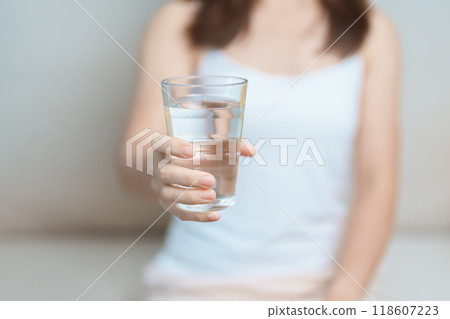 Happy woman holding water glass, female drinking pure water on sofa at home. Healthy, Refreshment, lifestyle and daily routine concept 118607223