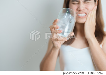 Teeth Sensitive to Cold concept. woman hold Ice Water glass and having toothache and pain after eat. Tooth Decay or Gum Disease, Grinding Teeth and Stress, Exposed Nerve Roots, Crack and Receding Gums Teeth Sensitive to Cold concept. woman hold Ice Water glass and having toothache and pain after eat. Tooth Decay or Gum Disease, Grinding Teeth and Stress, Exposed Nerve Roots, Crack and Receding Gums 118607262