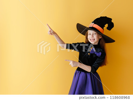 girl in Halloween witch costume on yellow wall background 118608968