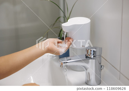 Little girl wash hands in bathroom. Kid use automatic soap dispenser. Hand with soapy solution closeup Little girl wash hands in bathroom. Kid use automatic soap dispenser. Hand with soapy solution closeup 118609626