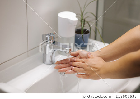 Female washing hands in bathroom sink at home checking temperature touching running water with hand Female washing hands in bathroom sink at home checking temperature touching running water with hand 118609633