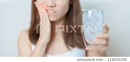 Teeth Sensitive to Cold concept. woman hold Ice Water glass and having toothache and pain after eat. Tooth Decay or Gum Disease, Grinding Teeth and Stress, Exposed Nerve Roots, Crack and Receding Gums Teeth Sensitive to Cold concept. woman hold Ice Water glass and having toothache and pain after eat. Tooth Decay or Gum Disease, Grinding Teeth and Stress, Exposed Nerve Roots, Crack and Receding Gums 118610280