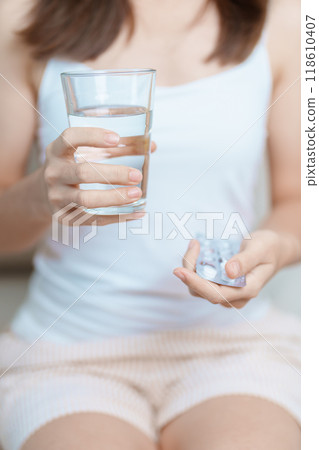 woman hand holding medicine painkiller pill and water glass on the sofa at home, taking for headaches, stomach ache, Diarrhea Pain from food poisoning, Endometriosis, Hysterectomy and Menstrual 118610407