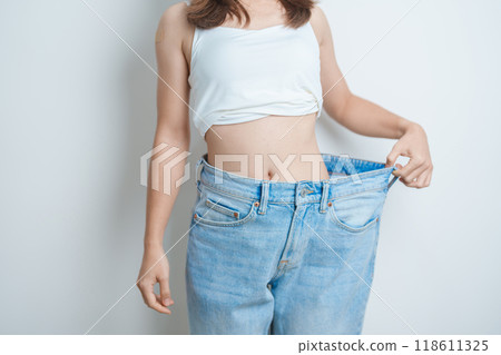 young slim female wearing big or oversize jeans, woman show healthy shape after weight loss. dieting, exercise, body fit and liposuction surgery concept 118611325
