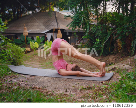 Beautiful woman practices yoga by pool in morning in Thailand. Young female in sportswear in hotel exotic garden. perfect flexible body recreating doing yoga poses feeling inner peace and vitality 118612329