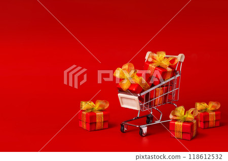 A shopping cart with red gifts with gold bows on a red background. Holidays, gifts, shopping copy space A shopping cart with red gifts with gold bows on a red background. Holidays, gifts, shopping copy space 118612532