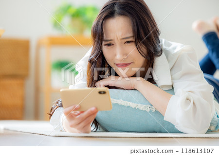 一位女士躺在客廳看她的智慧型手機 一位女士躺在客廳看她的智慧型手機 118613107