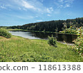 A serene river landscape surrounded by lush greenery and tall trees under a clear blue sky. 118613388
