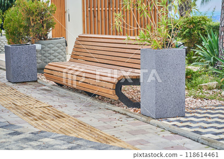 A wooden bench without people in a public park between flowerbeds with green plants and trees. There is a place to copy. High quality photo A wooden bench without people in a public park between flowerbeds with green plants and trees. There is a place to copy. High quality photo 118614461