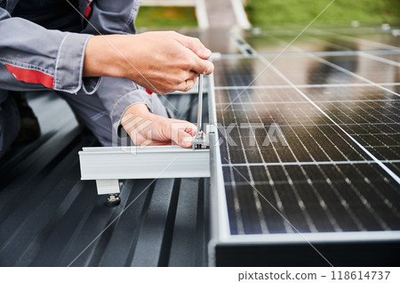 Man installer mounting photovoltaic solar panels on roof of house. Close up view of engineer installing solar module system with help of hex key. Concept of alternative, renewable energy. Man installer mounting photovoltaic solar panels on roof of house. Close up view of engineer installing solar module system with help of hex key. Concept of alternative, renewable energy. 118614737