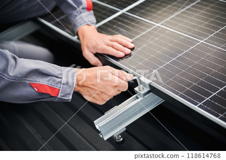 Close up view of installation of solar panel on roof. Worker securing PV battery frame by hexagon tool. Alternative energy source concept. Close up view of installation of solar panel on roof. Worker securing PV battery frame by hexagon tool. Alternative energy source concept. 118614768