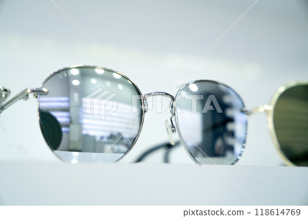 Close-up of round sunglasses with reflective silver lenses, highlighting stylish sleek modern design and metallic frames, fashion-forward accessories, minimalist display, retail ambiance 118614769