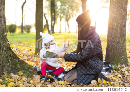 A mother is reading a book with her cute daughter while sitting on the lawn in the park A mother is reading a book with her cute daughter while sitting on the lawn in the park 118614942