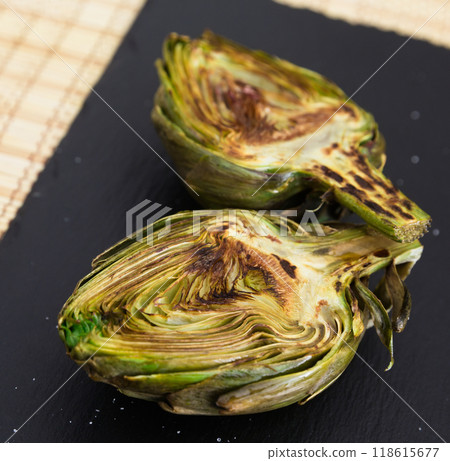 Cooked fried halves artichokes on black stone board 118615677