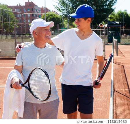 Grandfather and grandson talking on court playing tennis Grandfather and grandson talking on court playing tennis 118615683