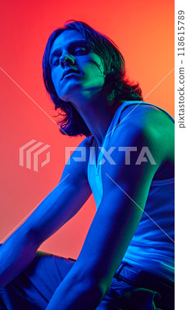 Posing in blue neon light young man showing himself through poses against gradient studio background. Uniqueness. Posing in blue neon light young man showing himself through poses against gradient studio background. Uniqueness. 118615789