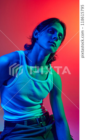 Portrait in blue neon light of young attractive man with long hair dressed casual outfit against gradient studio background. Portrait in blue neon light of young attractive man with long hair dressed casual outfit against gradient studio background. 118615795