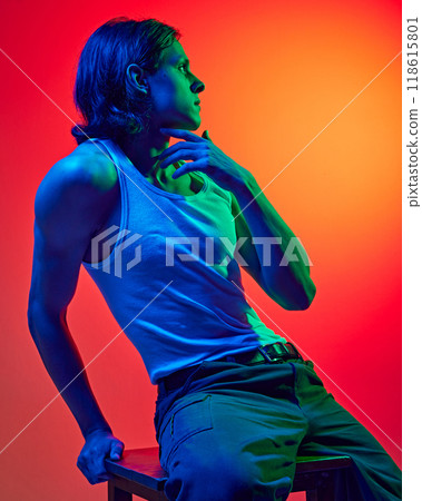 Stylish, attractive young man with athletic build body sitting on bar stool in blue neon light against gradient studio background. Stylish, attractive young man with athletic build body sitting on bar stool in blue neon light against gradient studio background. 118615801