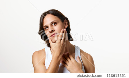 Young attractive brunette man, dressed white T-shirt touching his soft skin on chin after shaving against white studio background. Young attractive brunette man, dressed white T-shirt touching his soft skin on chin after shaving against white studio background. 118615861