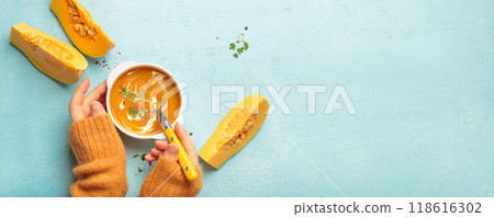 Woman holding spoon eating butternut squash soup with cream on blue background top view 118616302