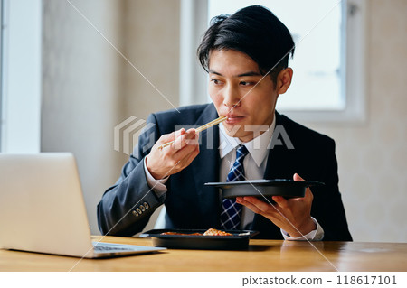 一個20多歲的年輕人，一邊吃便當一邊工作 118617101