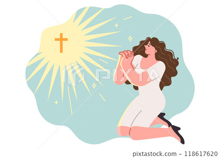 Christian woman prays to god on knees, near glowing catholic crucifix symbolizing faith in jesus 118617620