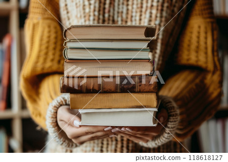 A girl in the library holds a stack of books in front of her 118618127