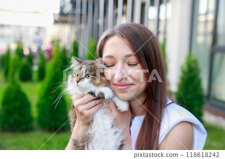 young woman lovingly cuddles her fluffy tabby cat outdoors, eyes closed in a moment of joy greenery young woman lovingly cuddles her fluffy tabby cat outdoors, eyes closed in a moment of joy greenery 118618242