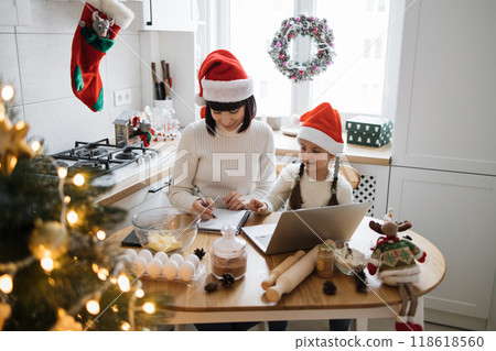 Mother and daughter baking Christmas cookies together in kitchen 118618560