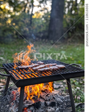 A barbecue grill with sizzling steaks over an open flame, set in a lush green outdoor setting 118618808