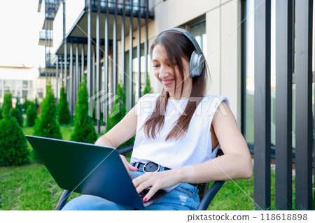 young woman wearing headphones works laptop outdoors Perfect for remote work 118618898