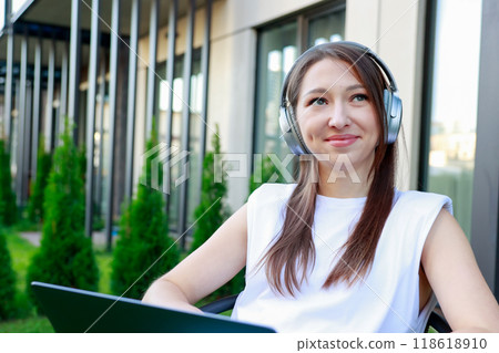 young woman wearing headphones works laptop outdoors Perfect for remote work 118618910